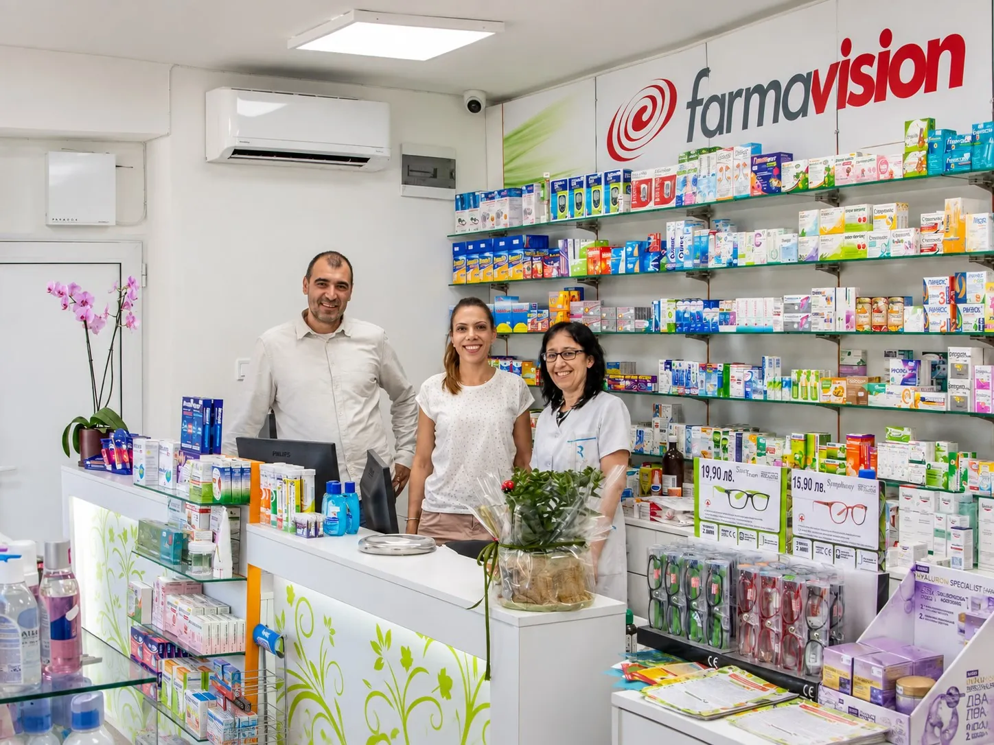 Екипът на обновена аптека зад касата, с рафтове за OTC продукти в търговската зала